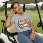 Woman wearing a grey t-shirt with 'I'd Rather Be Golfing' design, sitting in golf car.